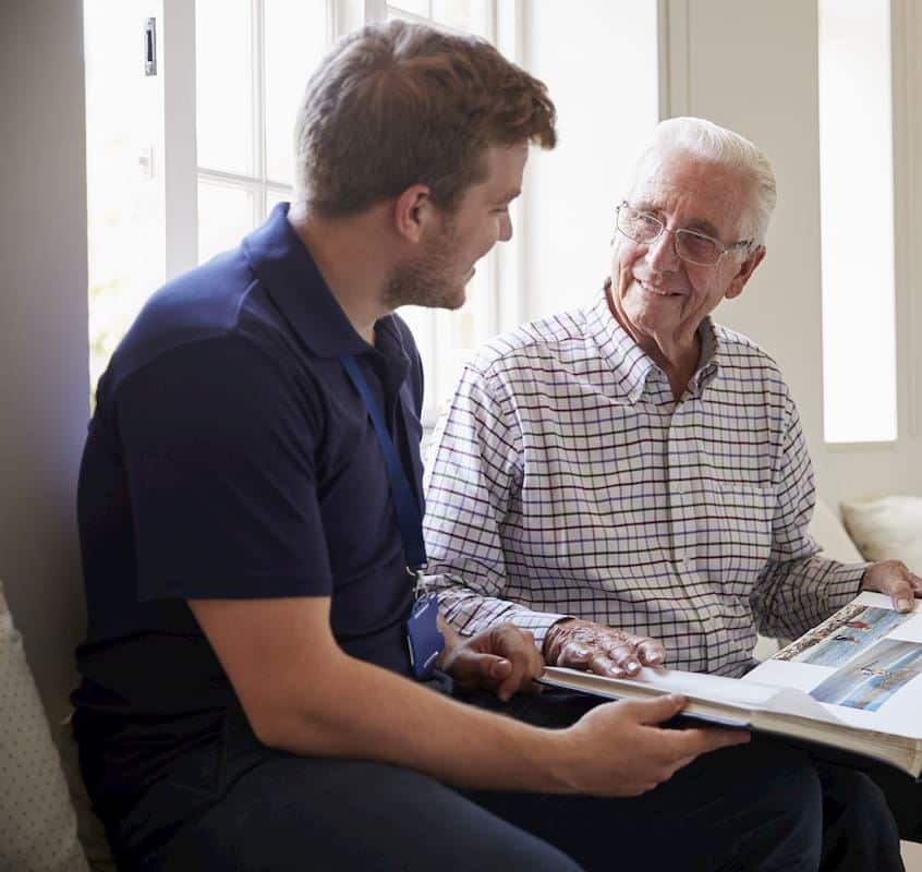 Senior man sitting looking at photo album with male nurse