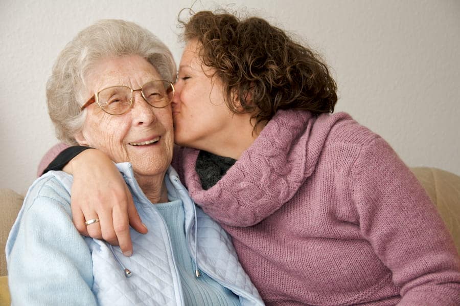 young woman giving smiling senior woman kiss on the cheek